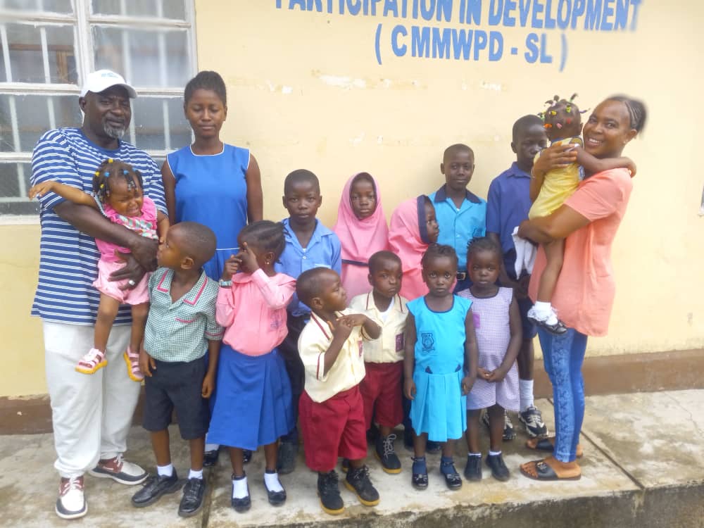 Schoolchildren in uniform with CMMWPD - SL staff outside a school in Bo District